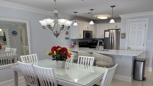 Una cocina moderna con una mesa de comedor de vidrio, sillas blancas, una araña y electrodomésticos de acero inoxidable.