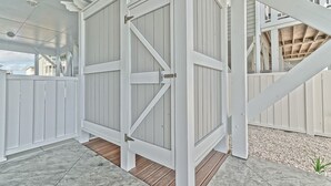 Un espace extérieur abrité, doté d’un portail en bois blanc, d’une terrasse en bois et d’un sol en pierre.