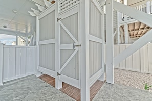 A covered outdoor area with a white wooden gate, a wooden deck, and a stone floor.