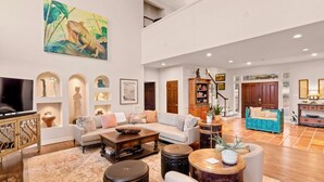 A spacious living area with a high ceiling, a large painting, and a variety of seating arrangements including a sofa, chairs, and a coffee table. - Retreat on the Pedernales River At Stone Home Ranch (Spicewood)