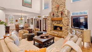 A spacious living room with a stone fireplace, comfortable seating, and a large TV. - Retreat on the Pedernales River At Stone Home Ranch (Spicewood)