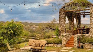 An outdoor seating area with a stone pergola, a cushioned bench, and a table. - Retreat on the Pedernales River At Stone Home Ranch (Spicewood)