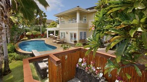 Ein zweistöckiges Haus mit Swimmingpool, einer überdachten Terrasse und üppigen tropischen Pflanzen.