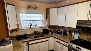 A kitchen with white cabinets, a granite countertop, a stove, a toaster, and a window with curtains. - Sunny Family Friendly 2 Bd1 Ba Sleeps 6, Safe, Fun & Walkable Grand Lake Oakland (Oakland)