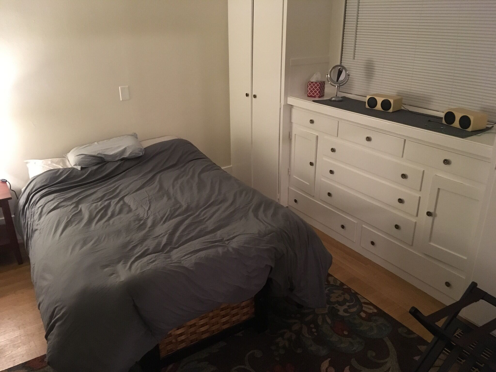 Una camera da letto con un letto, una cassettiera, uno specchio e un piccolo tavolo con degli altoparlanti.
