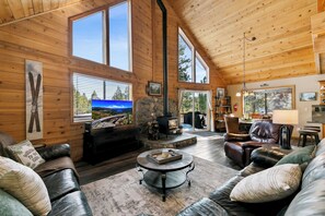A cozy cabin interior with a fireplace, leather furniture, and large windows offering views of the outdoors. - Tahoe Donner-Slp10, backs to XCountry, downhill skiing nearby. (Truckee)