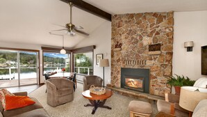 A spacious living room with a stone fireplace, comfortable seating, and a view of a lake. - Lakefront Paradise: Private Beach, Water Sports, Stunning Sunsets, Sleeps 8 (Bellingham)