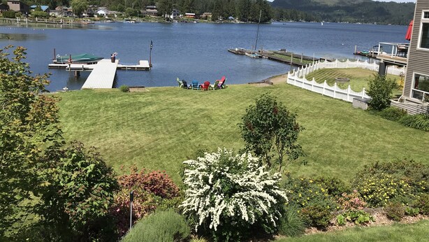 A lakeside property with a grassy lawn, dock, and dockside chairs. - Lakefront Paradise: Private Beach, Water Sports, Stunning Sunsets, Sleeps 8 (Bellingham)