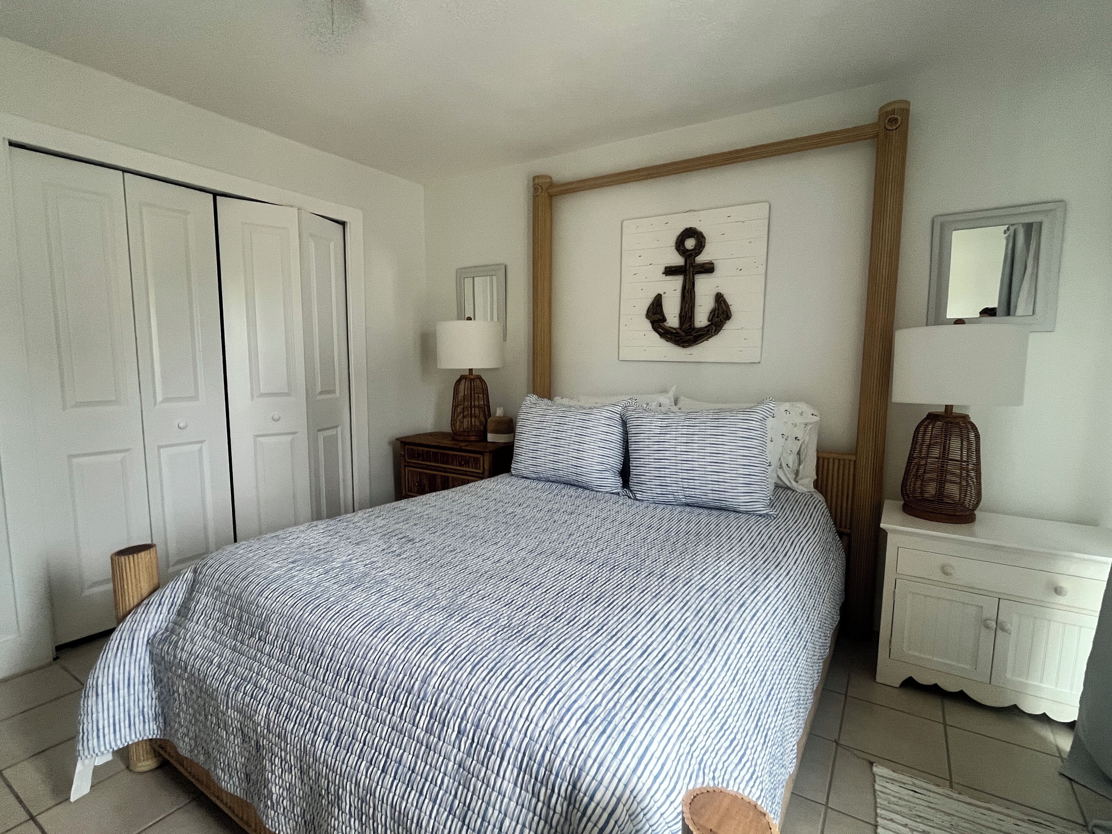 Une chambre à coucher comprenant un lit, une table de chevet, une commode, un miroir et un élément décoratif en forme d’ancre fixé au mur.
