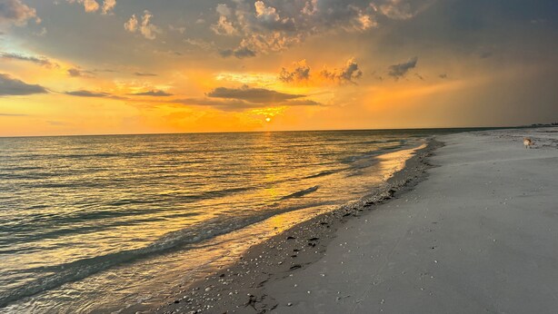Ein Strand mit Sonnenuntergang, ruhiger See und klarem Himmel.