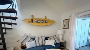 Ein Wohnzimmer mit einer Couch, einem Couchtisch, einer Surfbret-Dekoration, einer Treppe und einem Fenster mit Jalousien.