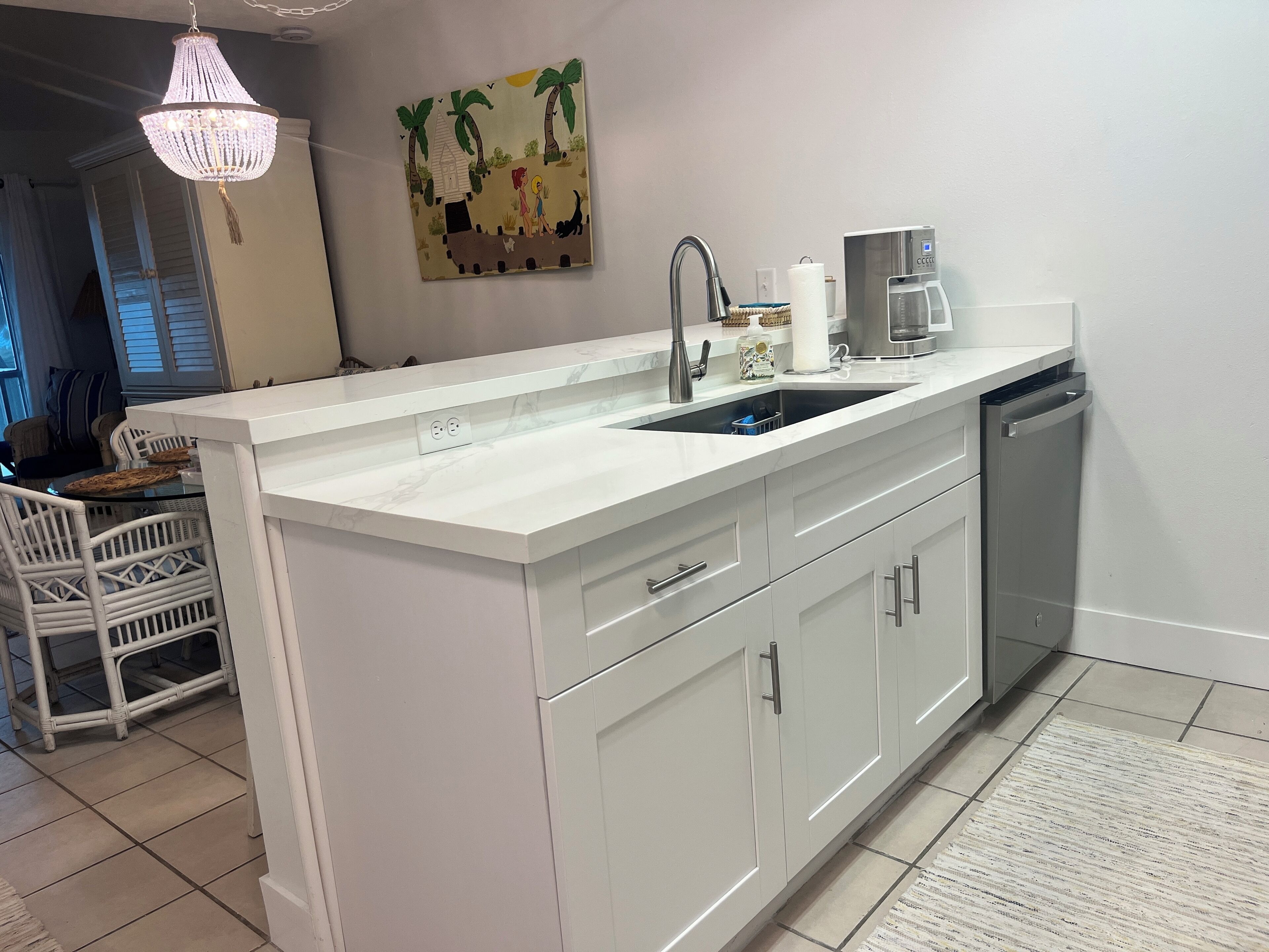 Una cocina moderna con encimera blanca, electrodomésticos de acero inoxidable y un cuadro decorativo en la pared.