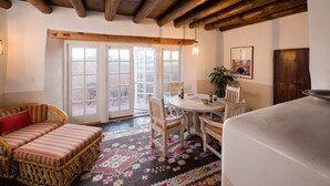 A cozy room with a wooden ceiling, a round dining table with chairs, a sofa with striped cushions, and a patterned rug. - Authentic Santa Fe Home~ Spacious, Vigas, Kiva Fireplaces and Walk to the Plaza (Santa Fe)