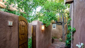 A narrow stone pathway leading to a wooden gate with a number 7 sign, surrounded by stucco walls and greenery. - Authentic Santa Fe Home~ Spacious, Vigas, Kiva Fireplaces and Walk to the Plaza (Santa Fe)