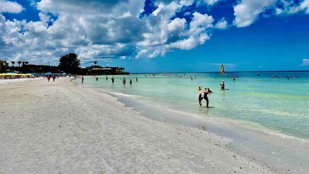 A beach with clear turquoise water, people swimming and walking along the shore, and a sailboat in the distance. - Star Fish. 3 Bed 2 Bath. POOL. Daily Rentals (Sarasota)