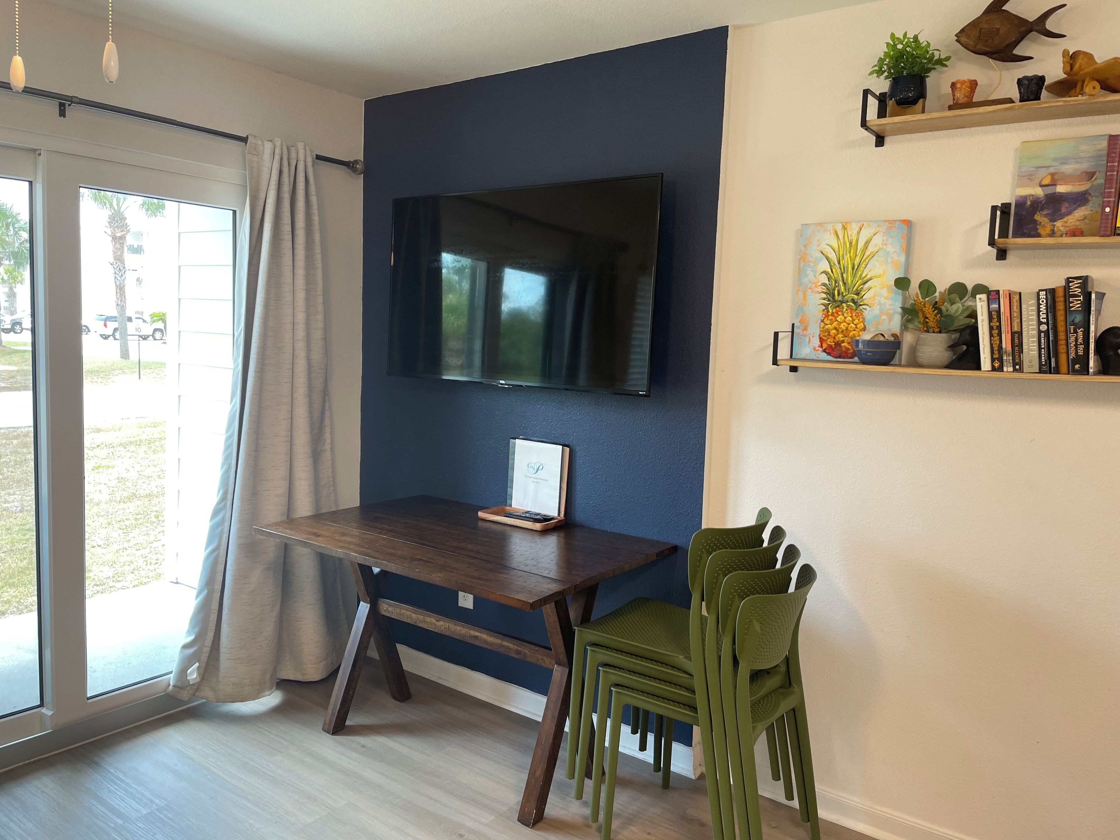 Una sala moderna con pared de acento azul oscuro, un televisor de pantalla plana montado sobre una mesa de madera y una silla verde.