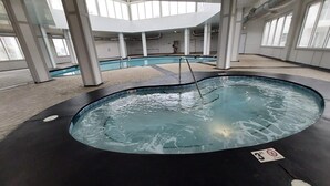 An indoor swimming pool with a black edge, surrounded by large windows and columns.