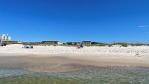 A beach with clear blue skies, sandy shore, and buildings in the background.