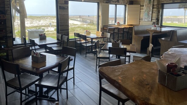 A restaurant with a rustic interior, large windows offering a view of the beach, and wooden tables and chairs.