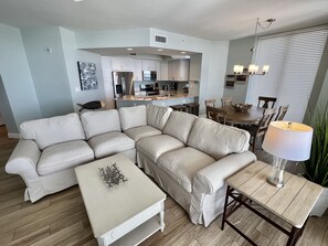 A modern living room with a sectional sofa, a coffee table, and a dining area with a wooden table and chairs.