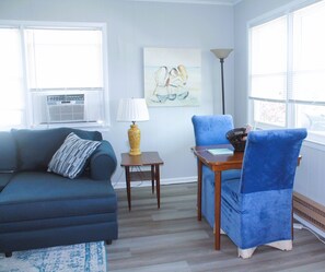 Ein Wohnzimmer mit einem blauen Sofa, einem blauen Sessel, einem kleinen Tisch mit einer Lampe und einem Bild an der Wand.