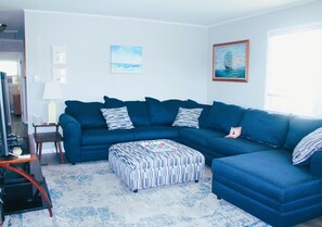 Ein Wohnzimmer mit einem blauen Ecksofa, einem gemusterten Hocker und einem kleinen Beistelltisch.