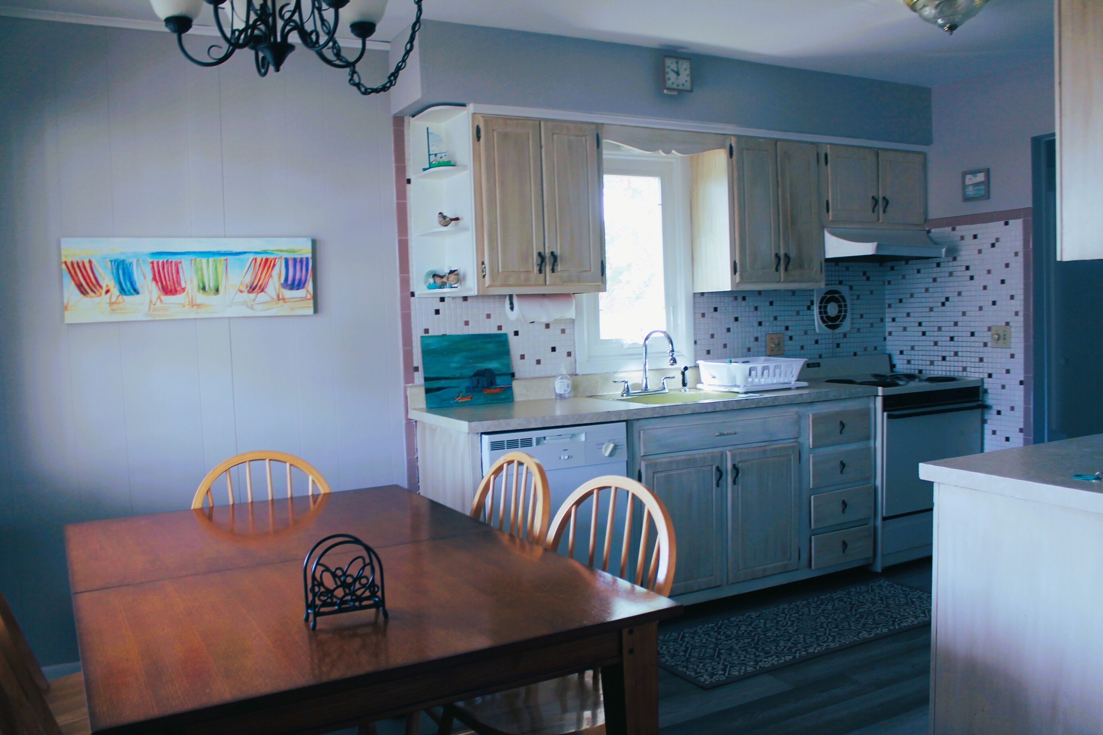 A kitchen with wooden cabinets, a dining table with chairs, and a colorful artwork on the wall.