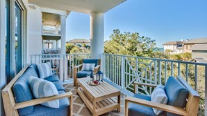 A balcony with a wooden table, two sofas, and a railing. - Stay on the Beach! Guest Favorite | Excellent Reviews | Chairs/Umbrella Included (Santa Rosa Beach)