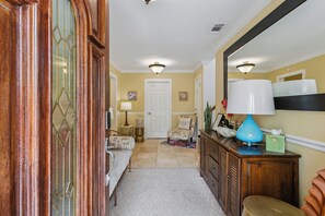 A hallway with a wooden door, a bench, a chair, a lamp, and a mirror on the wall.