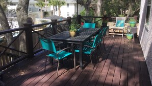 A wooden deck with a table and chairs, surrounded by potted plants and a large umbrella.