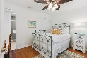 Een slaapkamer met een bed, een nachtkastje, een klok aan de muur en een plafondventilator.
