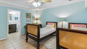 A bedroom with a bed, a nightstand, a lamp, a ceiling fan, and a bathroom visible through an open door.