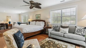 A well-lit bedroom with a large bed, a ceiling fan, and a view of the outdoors through the windows.