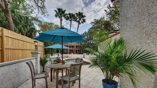 An outdoor patio with a wooden table and chairs, a blue umbrella, and a potted plant.