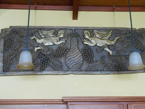 A wall with a decorative panel featuring cherubs and grapes, and two hanging bells.