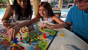 A group of people playing a board game at a table by a poolside.