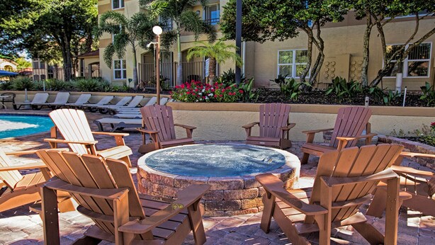 A poolside area with Adirondack chairs arranged around a hot tub, a pool, and a building with balconies in the background.