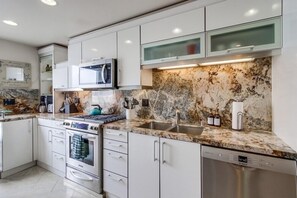 Kitchen features sleek cabinetry, microwave, stainless steel sink, dishwasher, and stove with kettle.