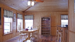 A wooden interior with a dining table, chairs, a bar area, and a bookshelf.