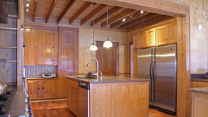 A modern kitchen with wooden cabinets, a stainless steel refrigerator, and pendant lighting.