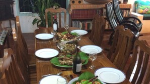 A dining table set with plates, glasses, and a bottle of wine, surrounded by wooden chairs.