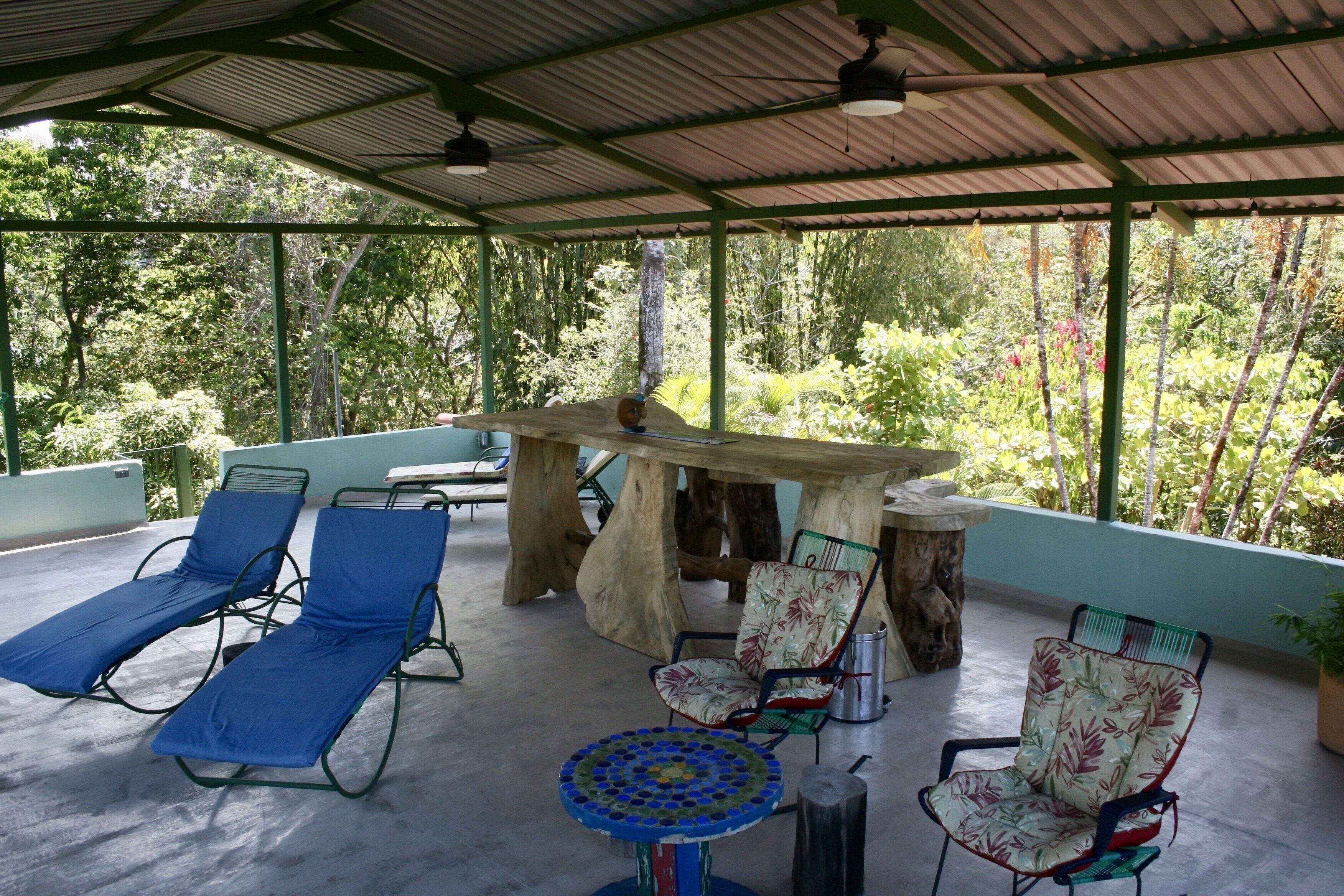 Een overdekt terras met loungezetels, een tafel en stoelen.