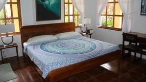 A bedroom with a wooden bed, a nightstand, a chair, and a window with curtains.