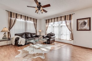 Ein Wohnzimmer mit einer Ledersofa, einem Glastisch und einem Deckenventilator.