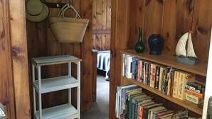 A wooden interior with a bookshelf, a wicker basket, and a small table. - Cape Cod Pond Cottage (Eastham)