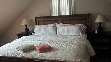 A bedroom with a wooden bed, two bedside tables with lamps, a window with curtains, and a sloped ceiling.