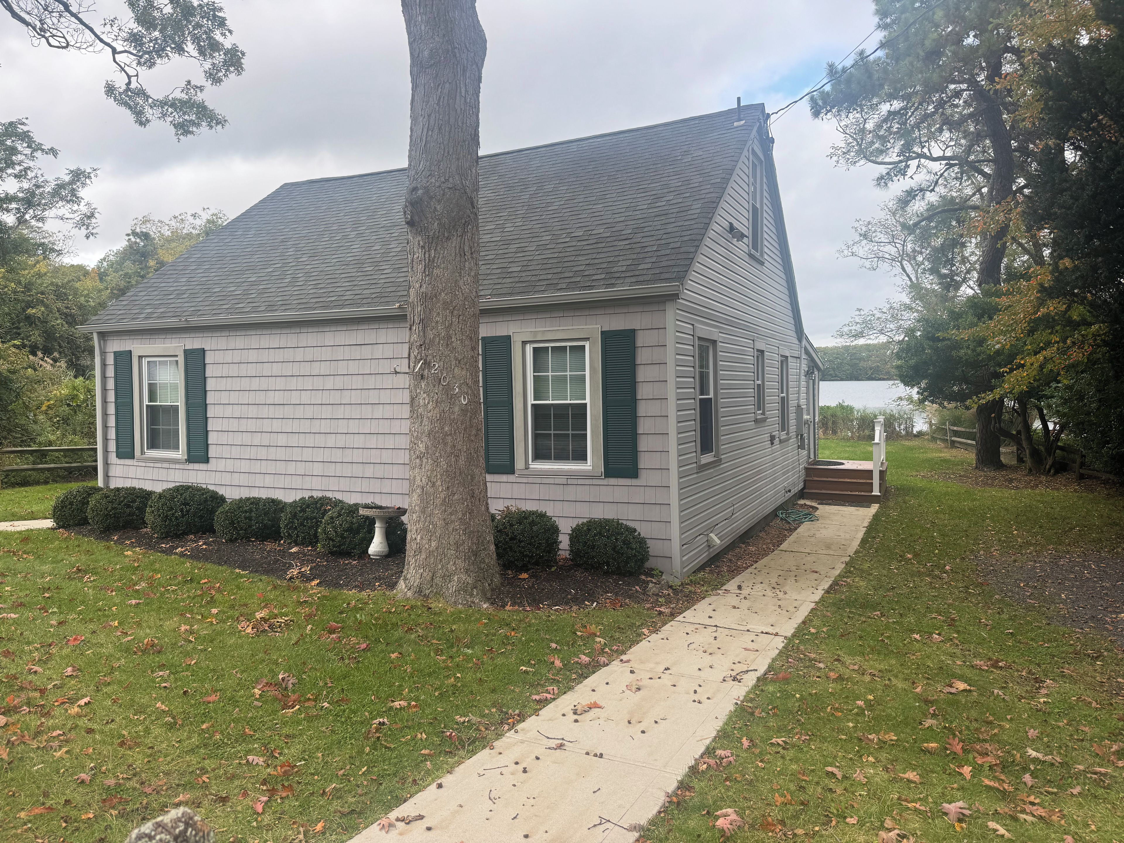 A single-story house with a grey shingled roof, green shutters, and a white door.