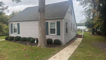 A single-story house with a grey shingled roof, green shutters, and a white door.