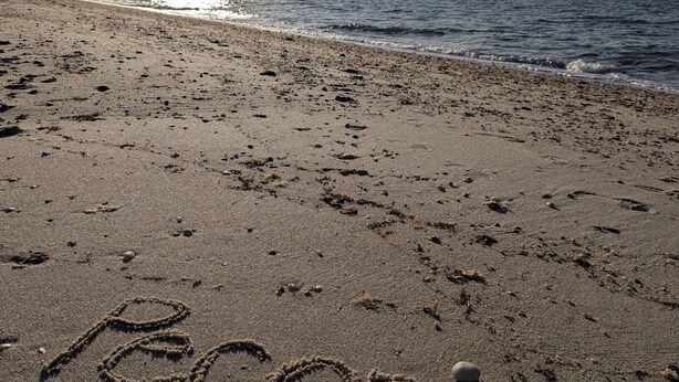 En strand med fodspor og ordet "Reconcili" skrevet i sandet.