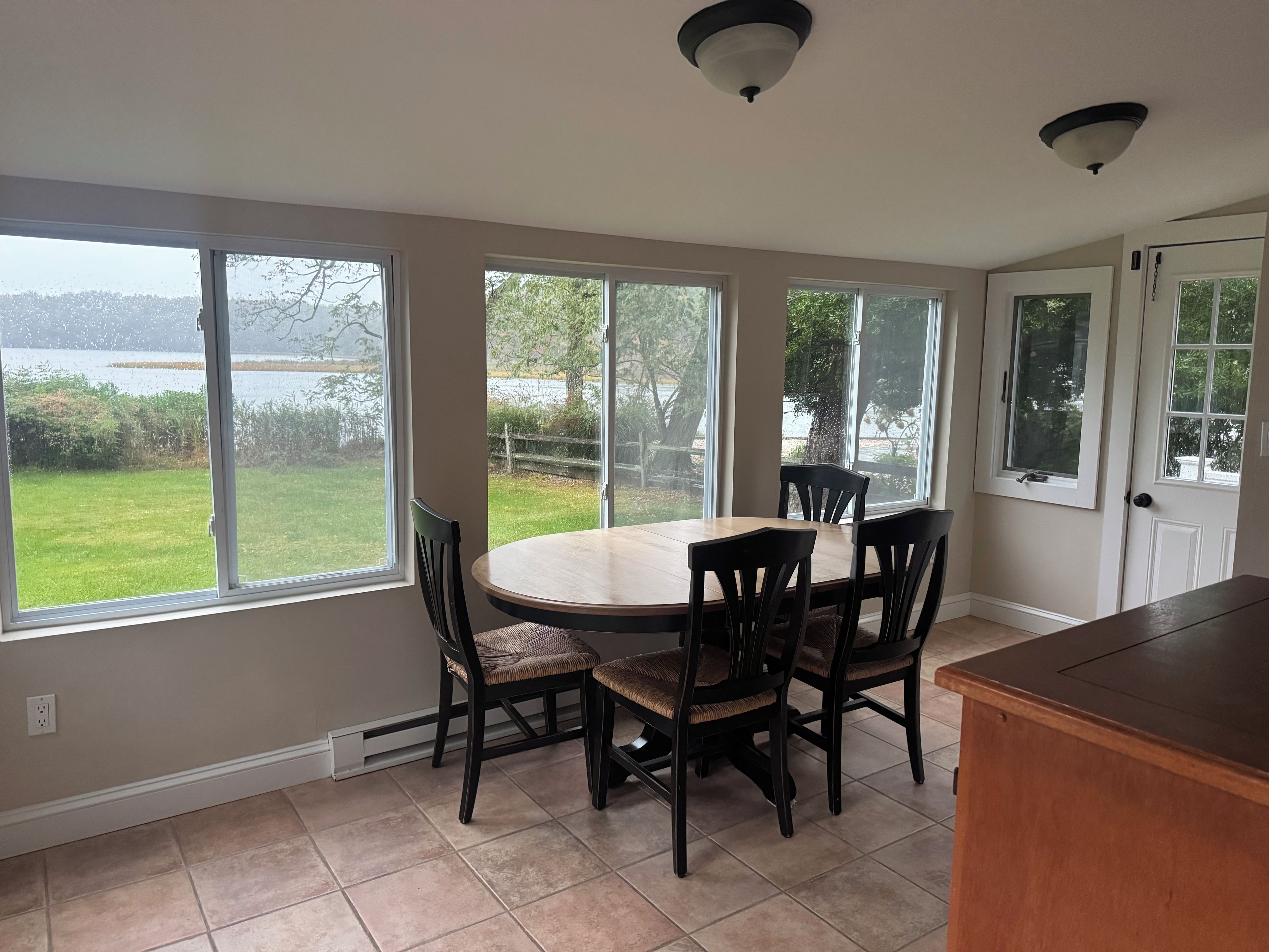 A kitchen with a dining table and chairs, large windows, and a view of a lake.